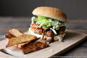 The kotlet burger is filled with a kotlet, lettuce, tomato and lots of barbecue sauce, with golden potato wedges on the side.