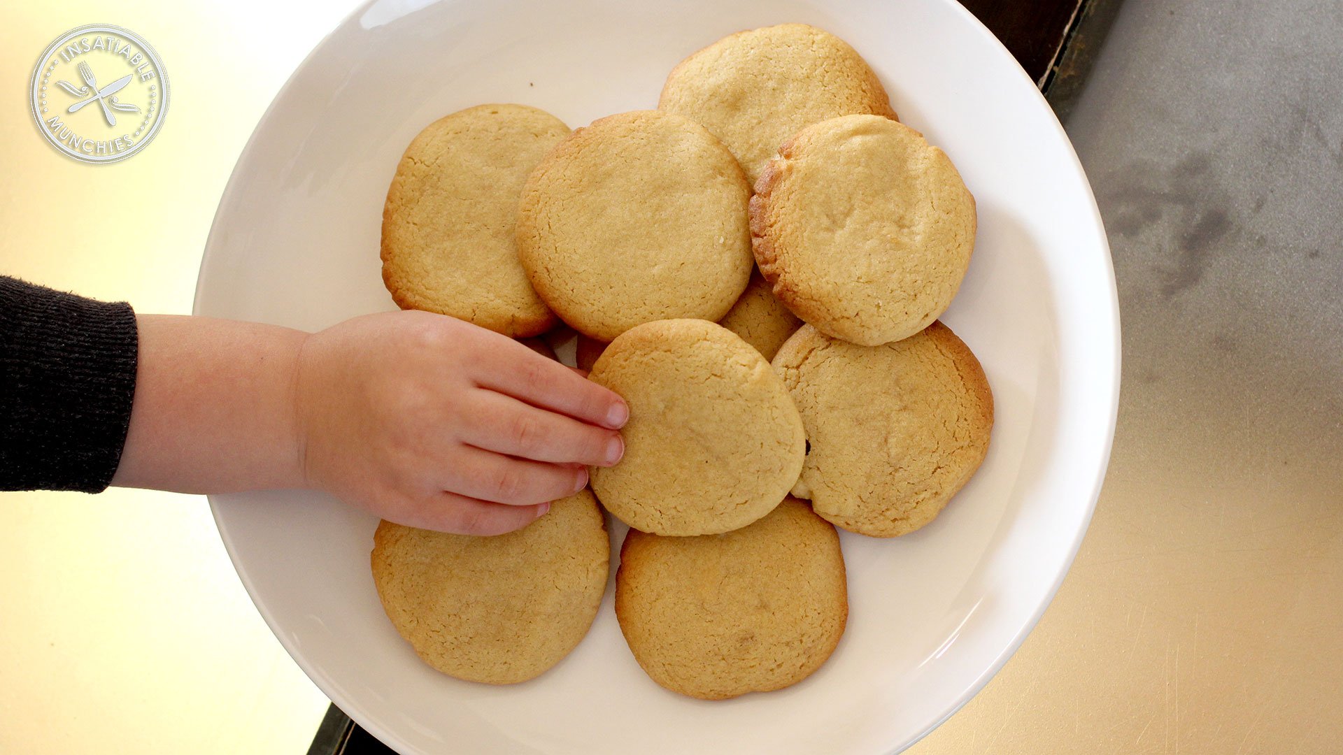 a little hand reaching for a cookie from a pile on the plate.