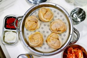 Korean style kimchi dumplings are steamed and served with a side of soy, pickled radish, and freshly marinated cabbage.