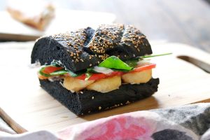 Shrimp sandwich made with battered shrimp, kewpie mayo, tomato, lettuce, on black squid ink bread.