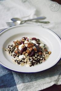A salad of black rice and pearl cous cous, served with a roasted garlic and tahini dressing, greek yoghurt, baby beetroot and smoked almonds. Here, it's served on a blue-rimmed tin plate and laid next to a fork and spoon, on a blue tea towel.