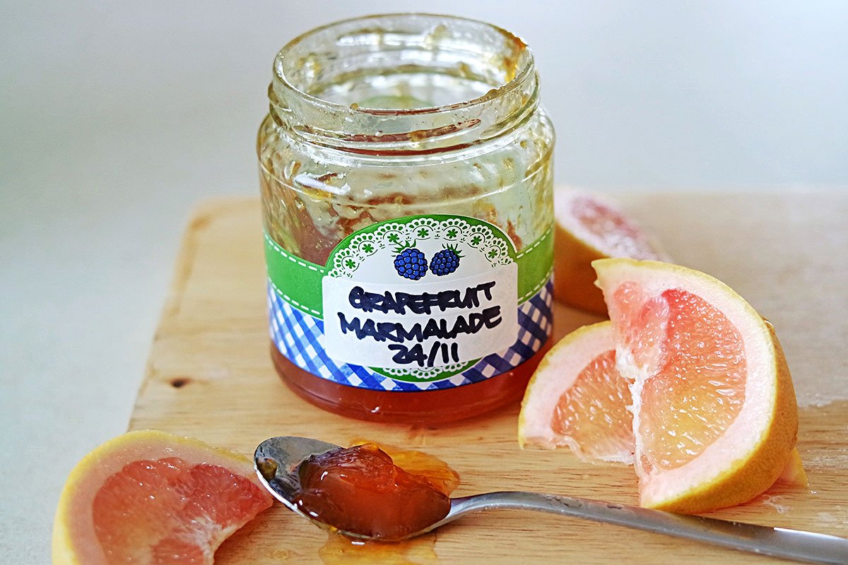 Finished Jar of Grapefruit Marmalade sitting on a board, open, with fresh wedges of grapefruit.