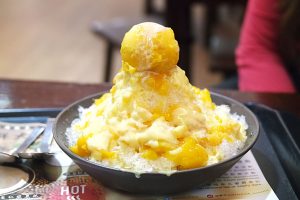 A tower of crushed ice is surrounded by fresh cut mango, and topped with a mango sorbet, and a drizzle of evaporated milk