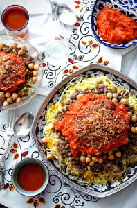 A plate of Koshari sits on a table set with smaller plates, cutlery, and middle easter inspired napkins