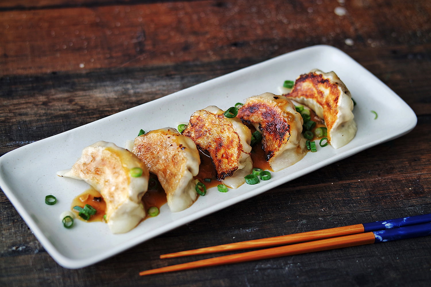 Shiitake Mushroom Gyozas, lined up on a long plate and garnished with a miso dipping sauce and finely chopped green spring onions