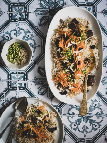 A platter of afghan braised lamb and rice, topped with candied carrots and pistachios, with a serving removed to the side.