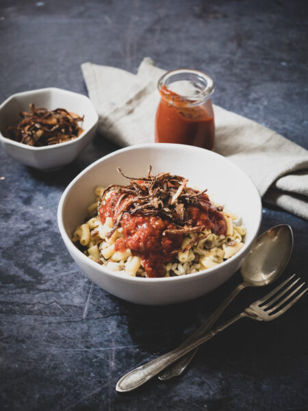 A bowl of koshari served topped with a spiced tomato based sauce and fried onions.