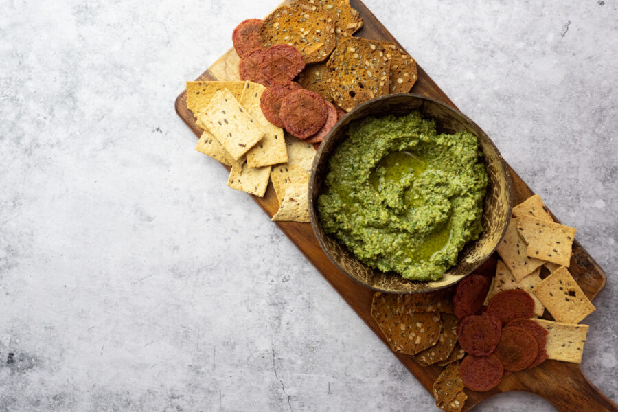 A bowl of pesto served on a wooden board with crackers