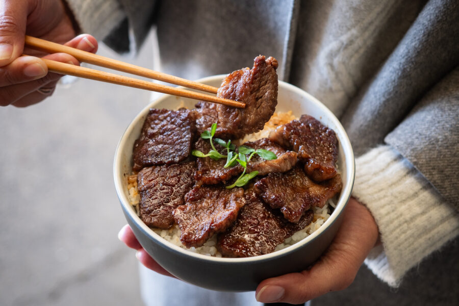 A piece of beef lifted by chopsticks on a bowl of rice
